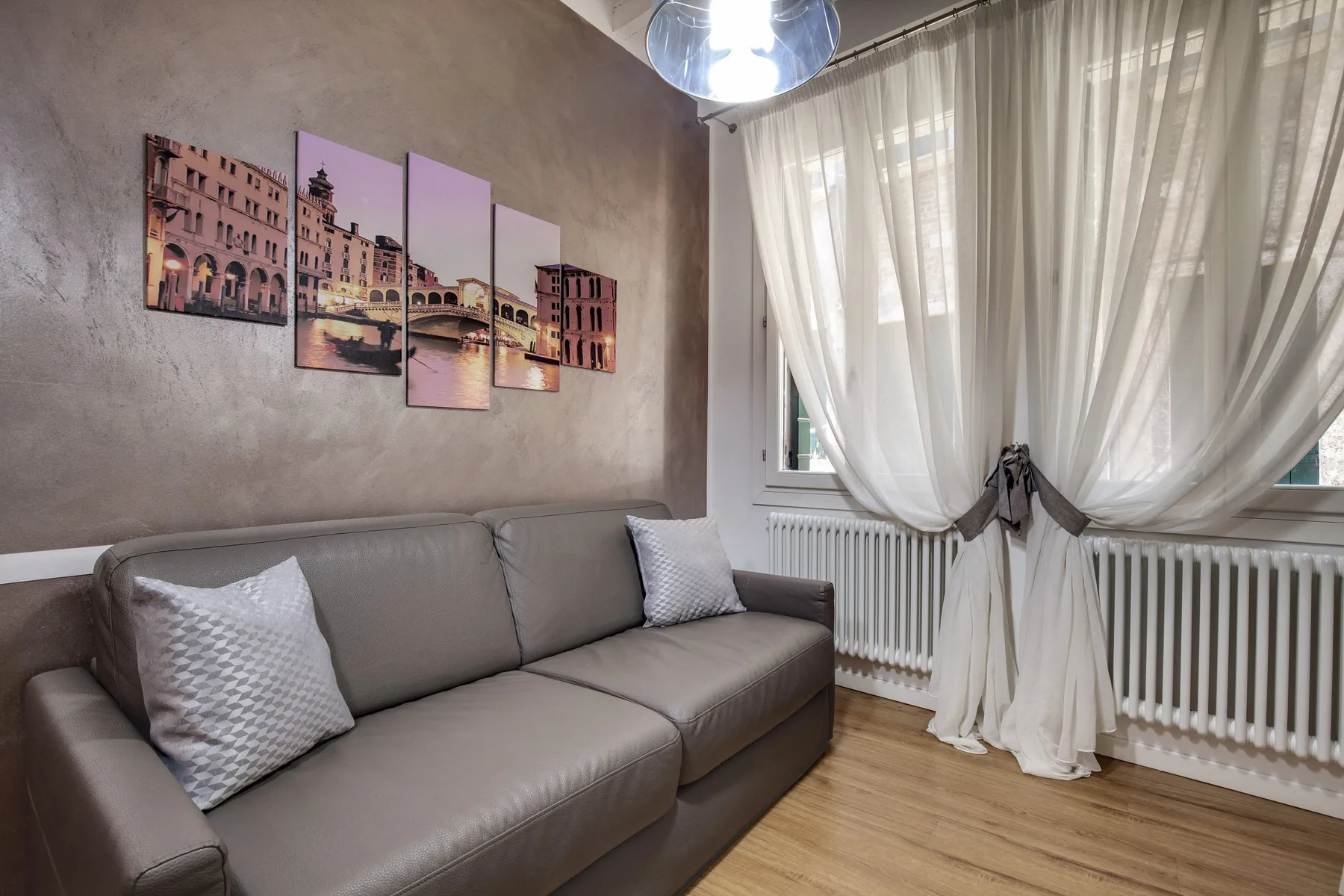 Una sala de estar con un sofá gris y cortinas translúcidas sobre la ventana.