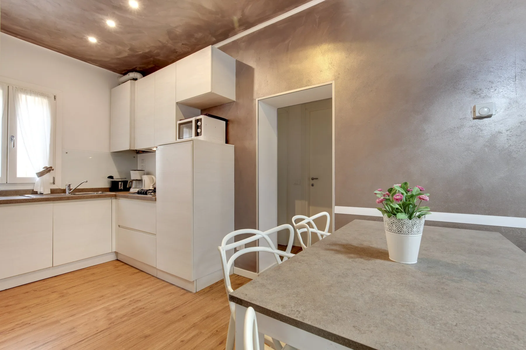 Comedor junto a una cocina compacta, con una mesa y flores en una maceta.