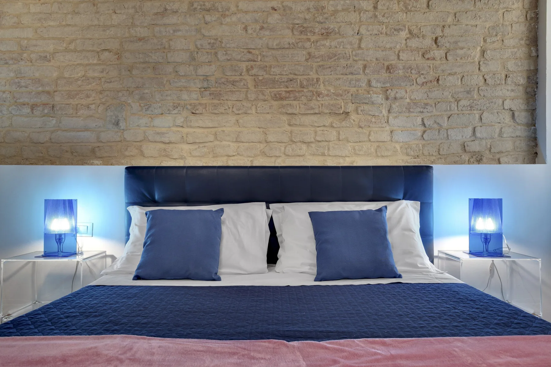 Un dormitorio con una cama bien tendida y lámparas azules junto a la cama.