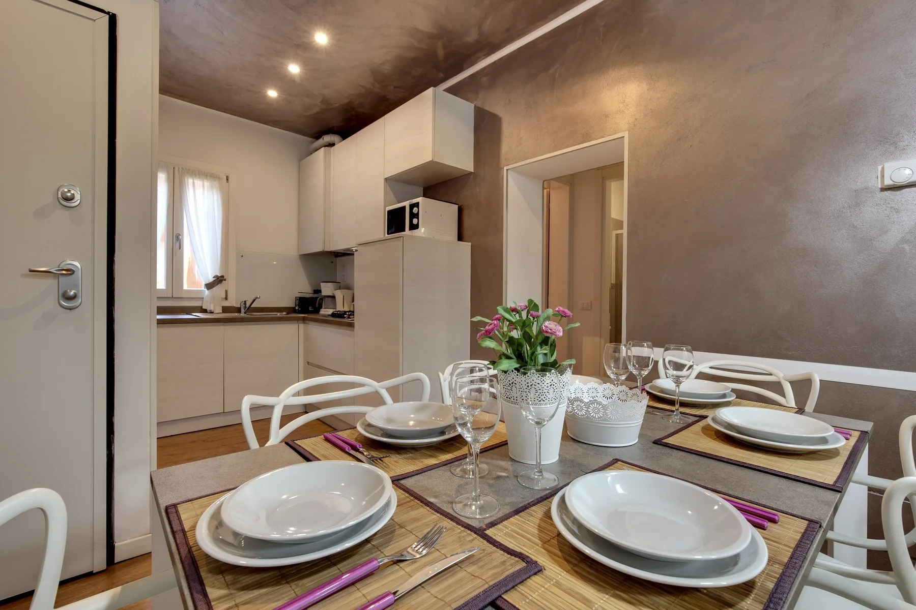Comedor con la mesa preparada y una cocina compacta al fondo.