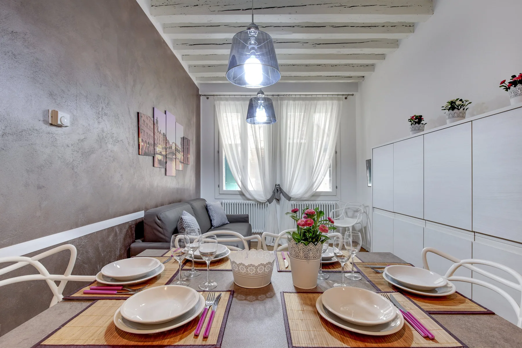 Un comedor con la mesa puesta junto a una zona de estar y armarios blancos.