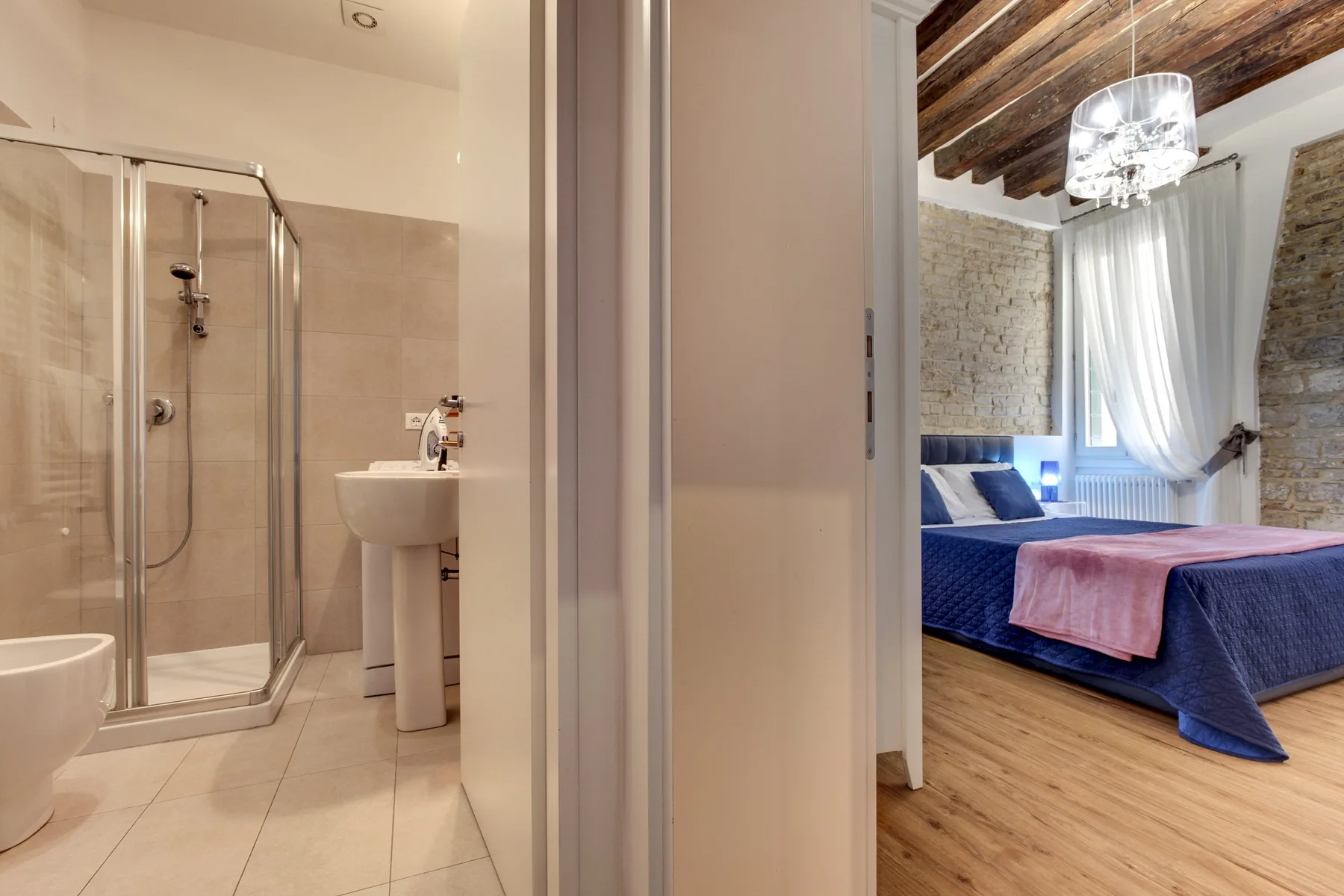Un baño con ducha de vidrio y lavabo da a un dormitorio con una cama.