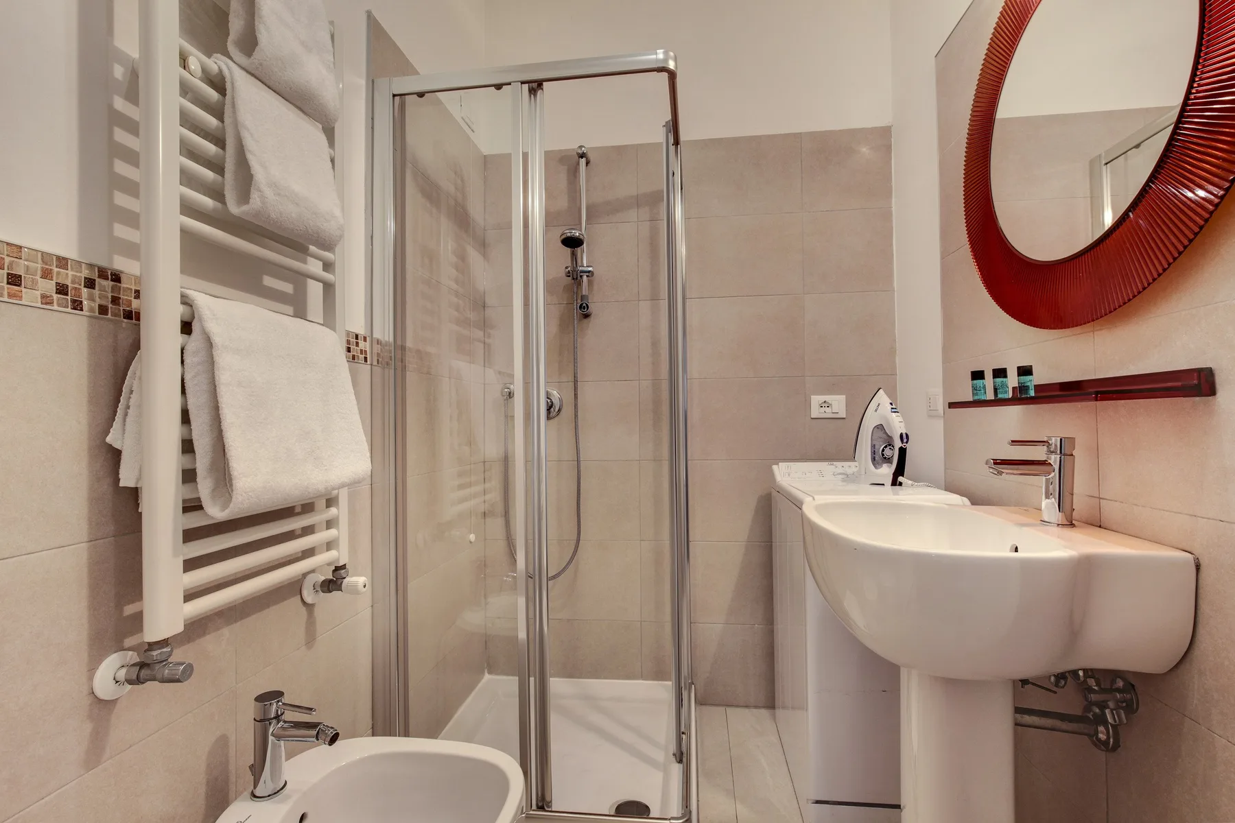 Un baño con ducha, lavabo y toallero calefactor de pared.