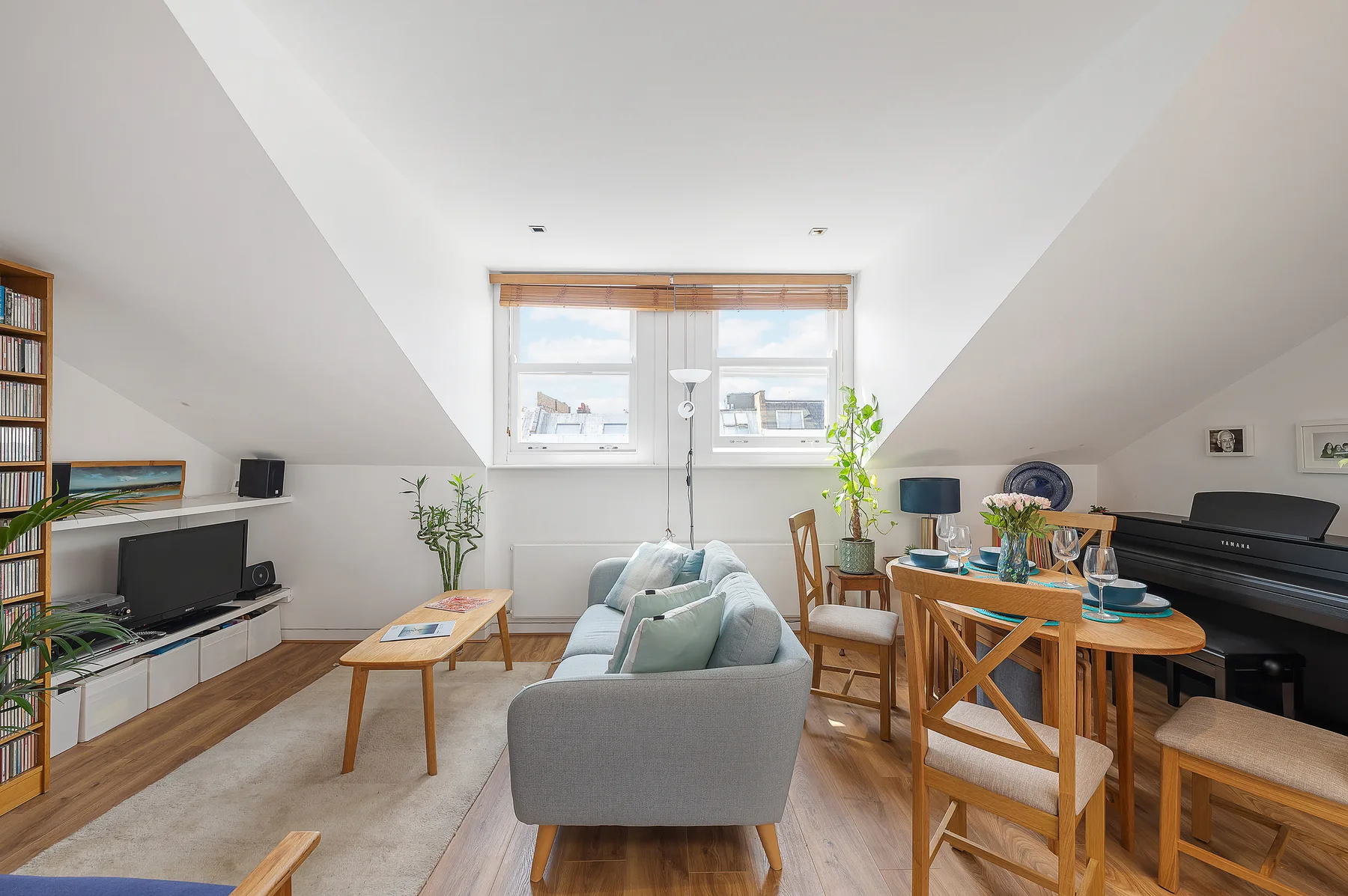 A bright attic living and dining area with seating, a table, and a keyboard.