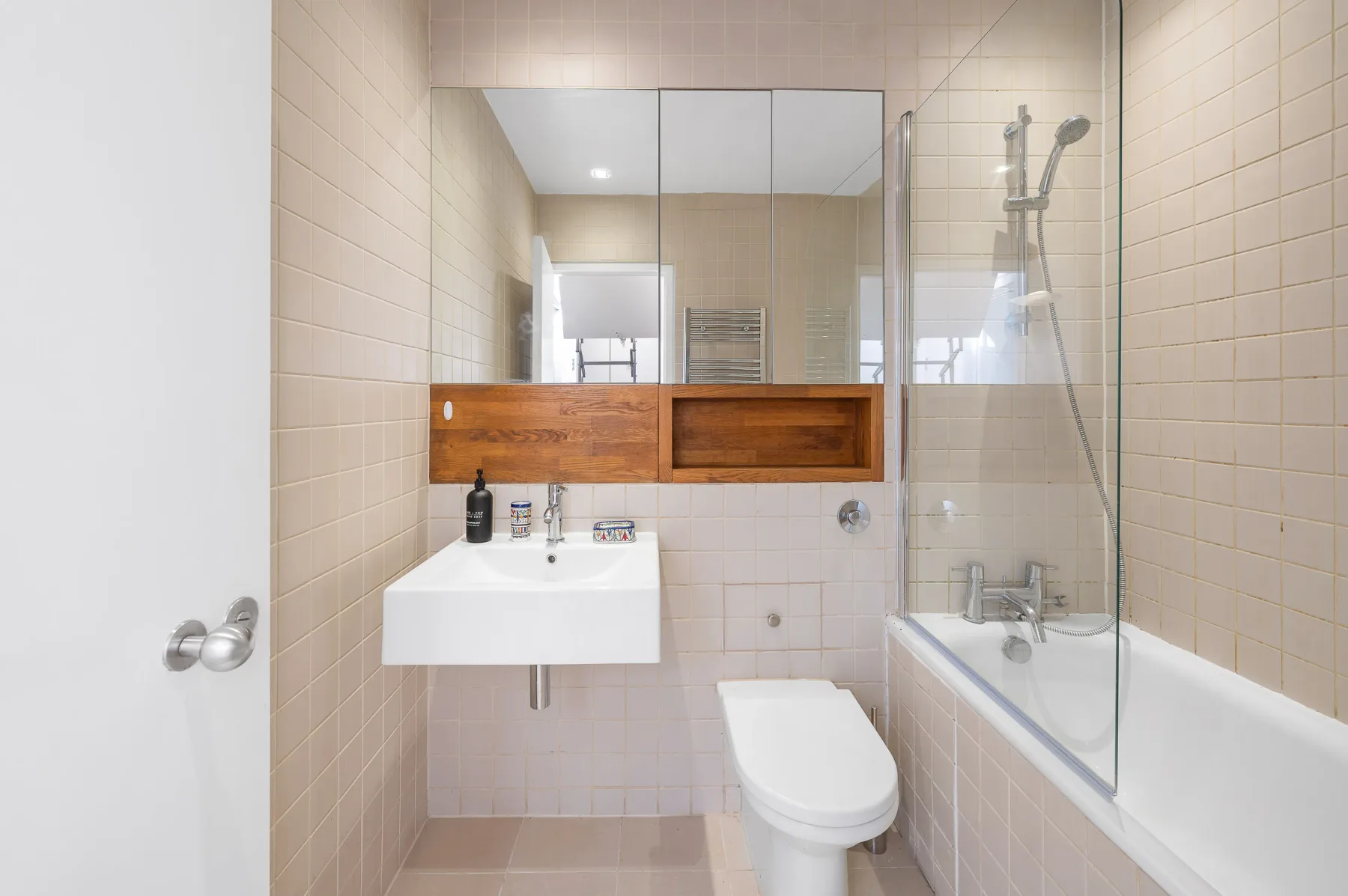 A tiled bathroom with a sink, toilet, and bathtub with a glass shower screen.