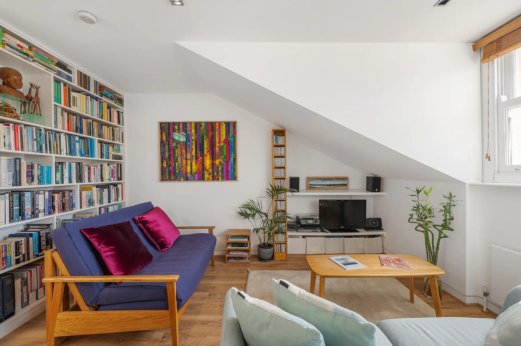 A bright living room with a blue seating area, bookshelves, and a television.