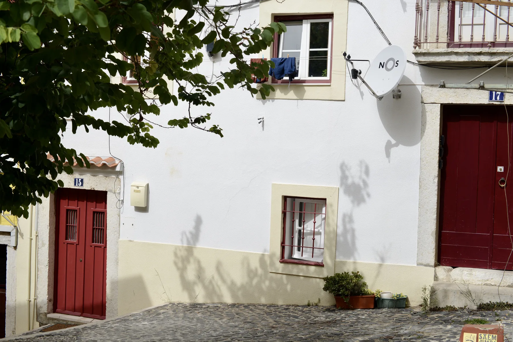 White residential facade with red doors and barred windows along a cobbled street.