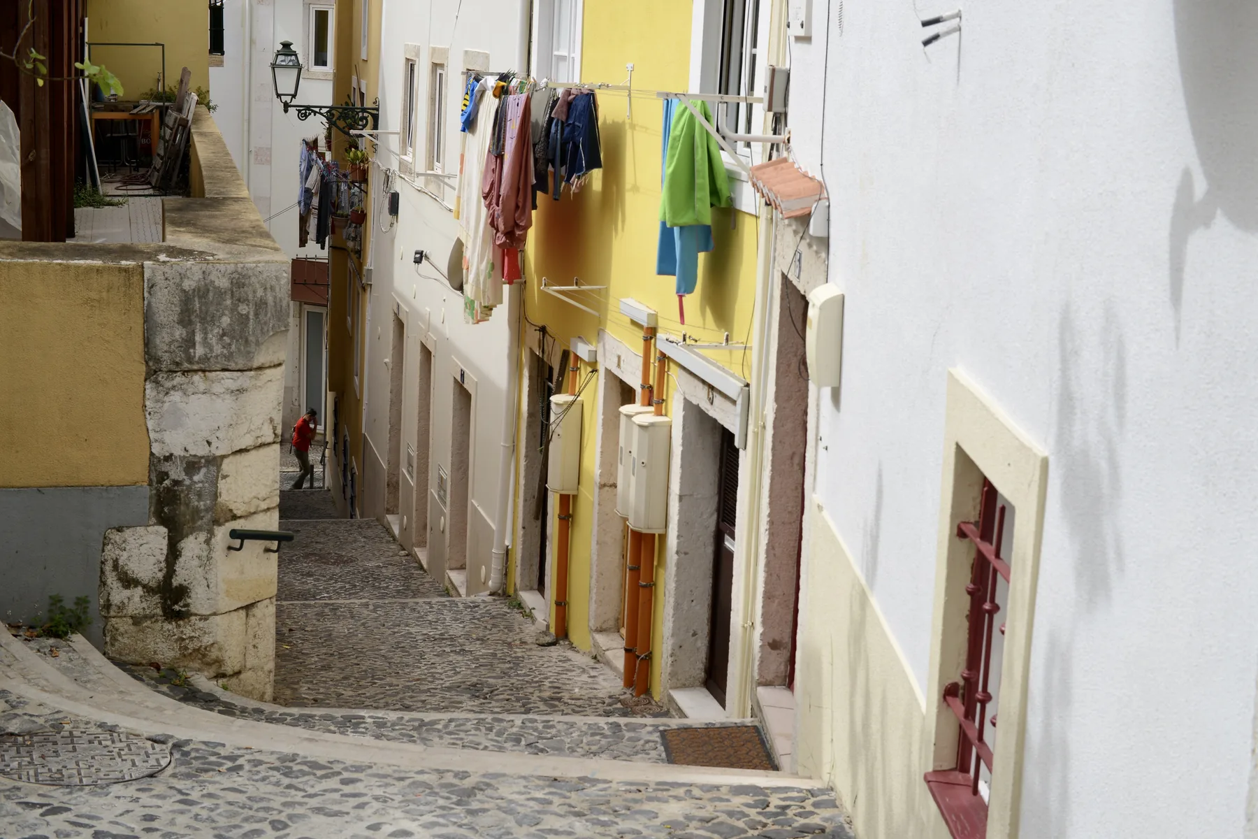A narrow cobblestone street runs between colorful buildings with laundry hanging overhead.