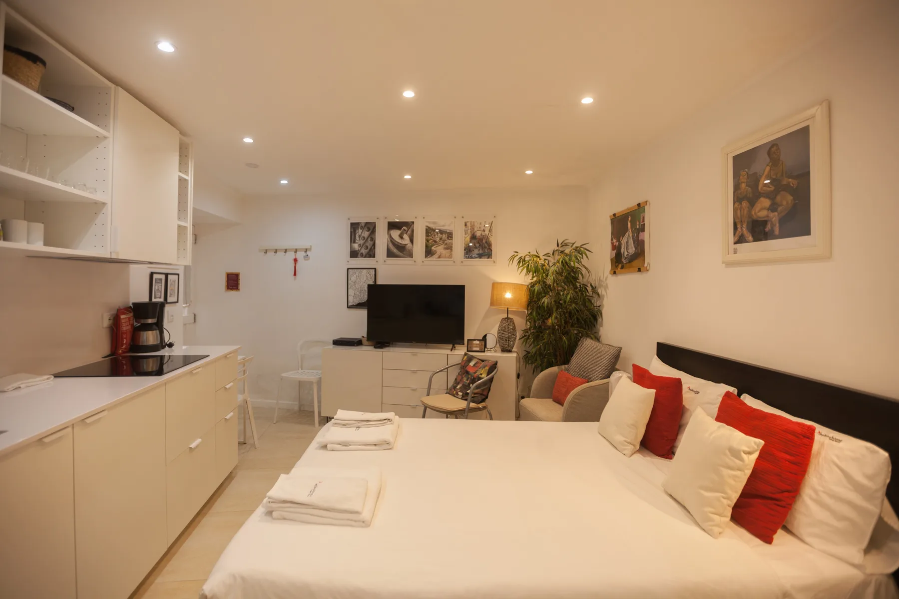 Studio room with a bed, kitchenette, and a seating area around a television.