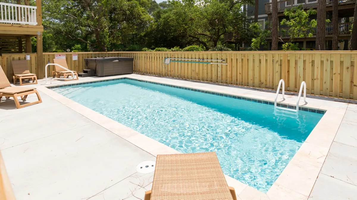 An outdoor swimming pool is surrounded by a paved deck and lounge seating.