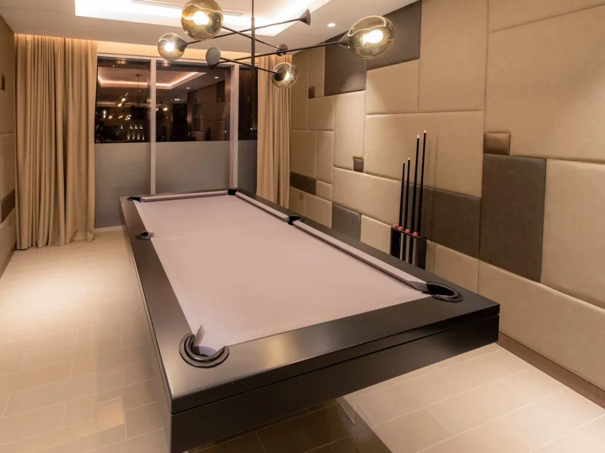 A billiards room with a pool table and cues beside the wall.