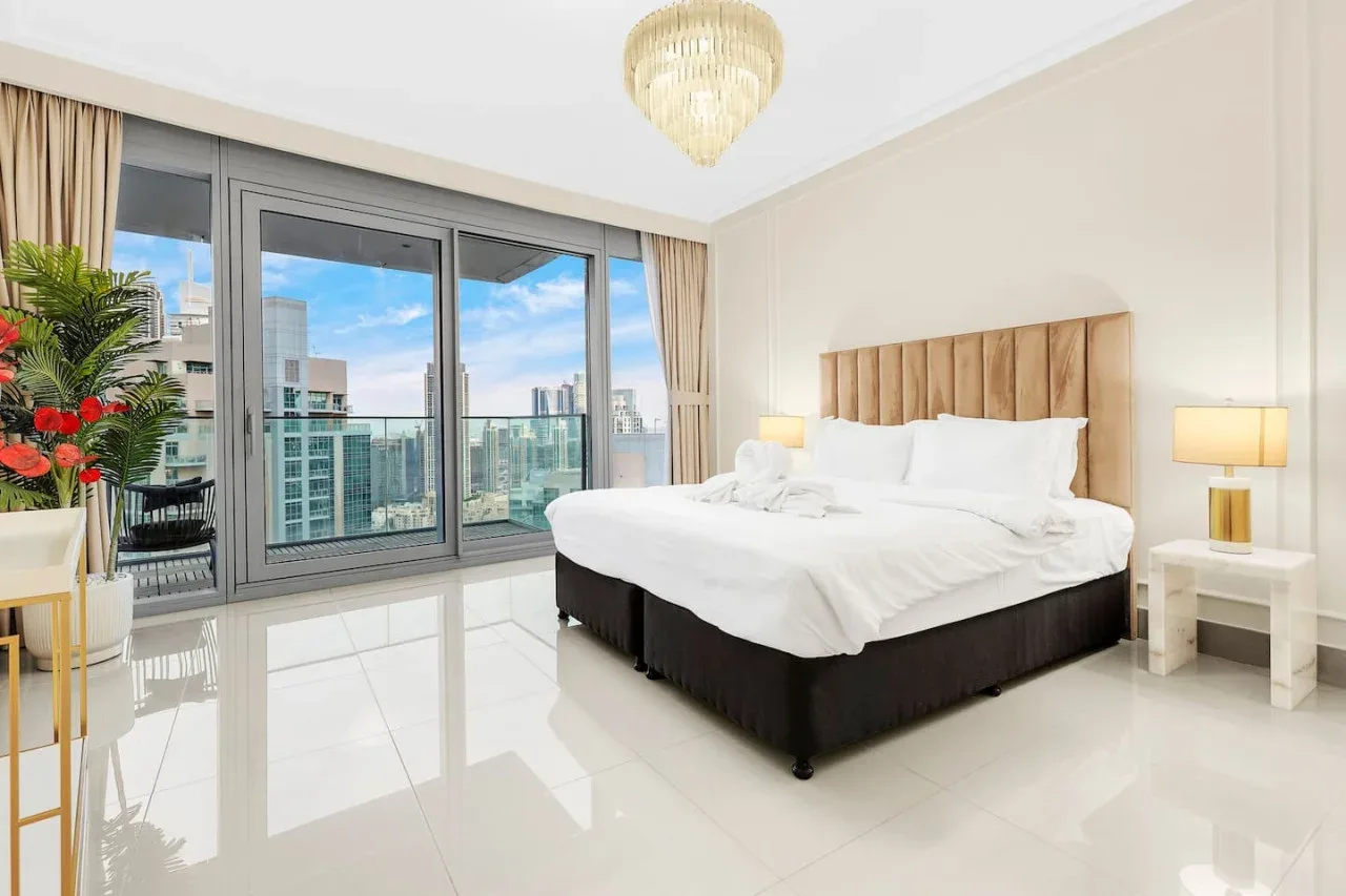 A bright bedroom with a large bed beside floor-to-ceiling windows.