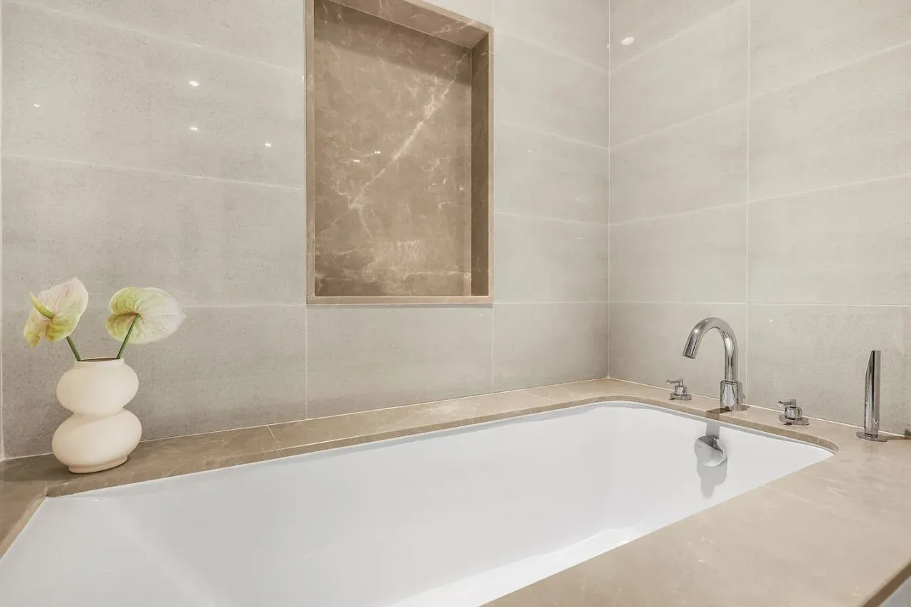 A bathtub sits beneath a recessed wall niche, with a vase on the ledge.
