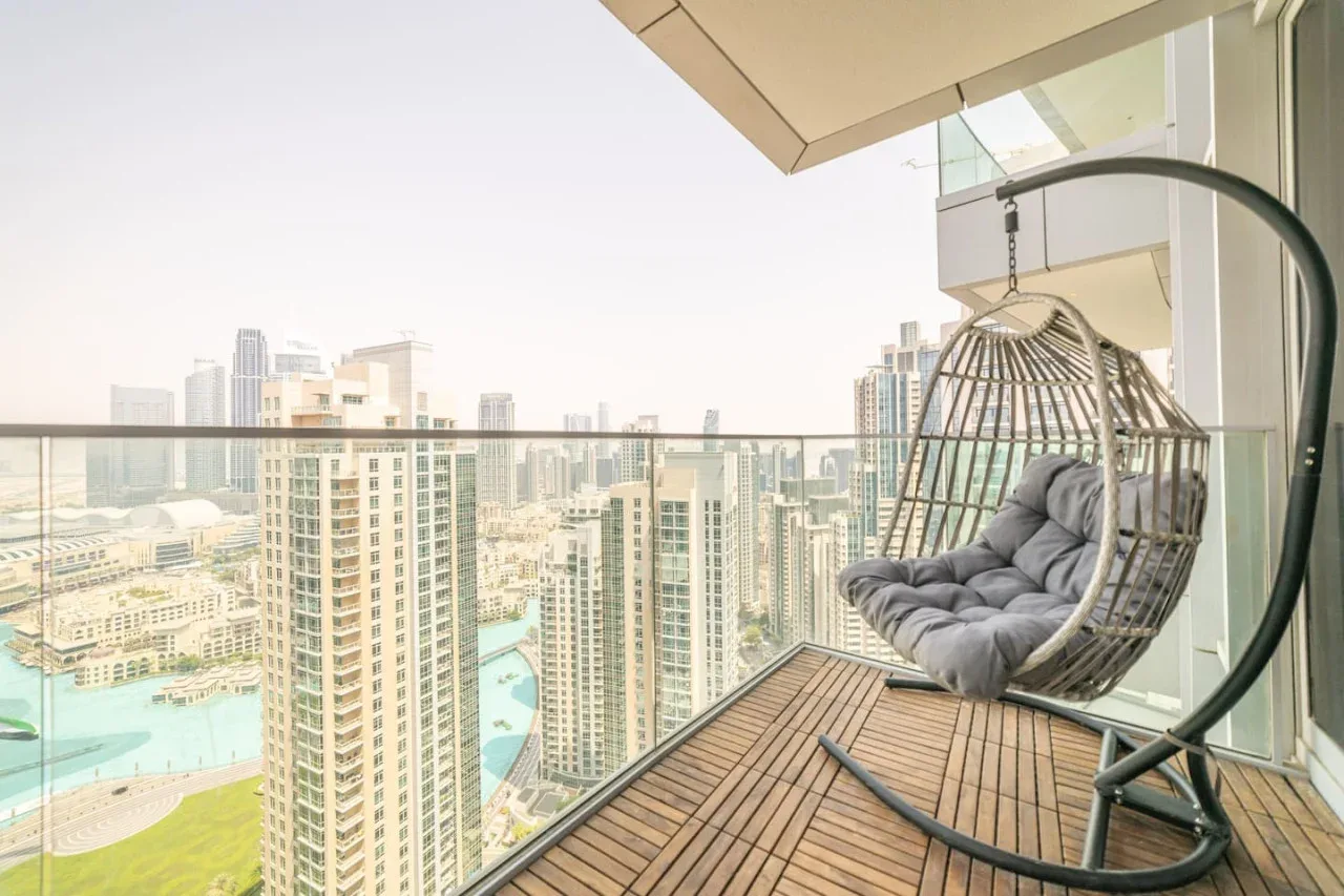 A balcony with a hanging cushioned seat overlooking high-rise buildings and a pool.