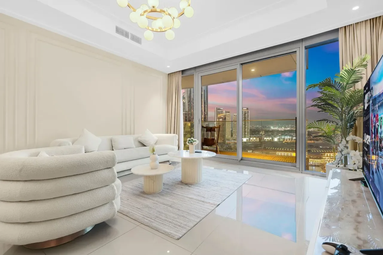 A bright living room with curved seating and large windows overlooking the city at sunset.