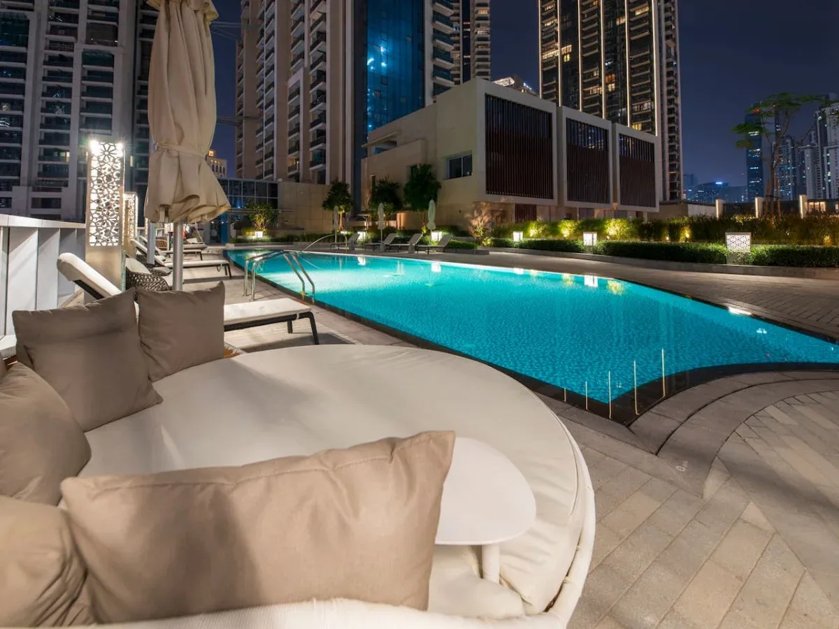A rooftop swimming pool beside cushioned lounge seating at night.