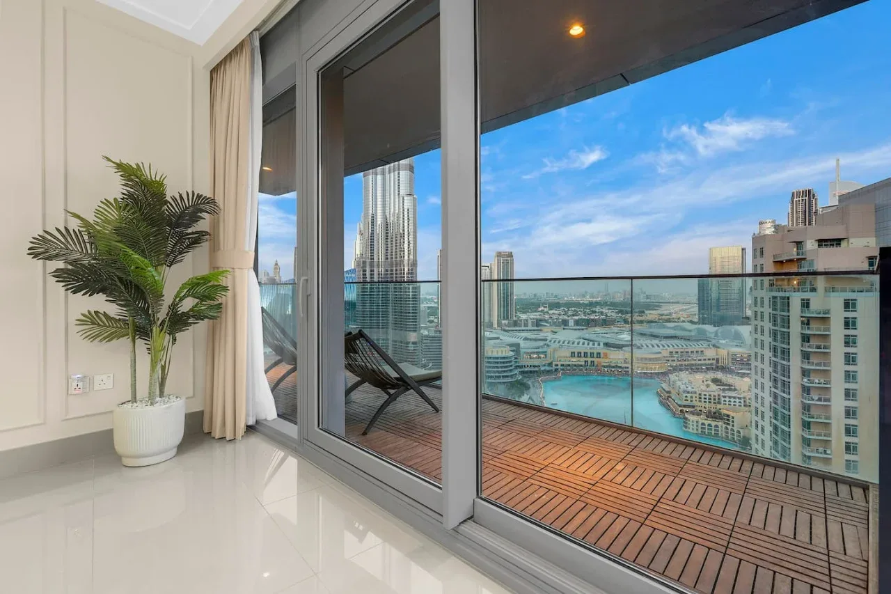 A bright interior opens onto a balcony with a city and water view.