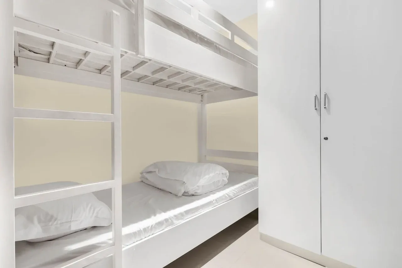 A bright bedroom with white bunk beds and a tall wardrobe.