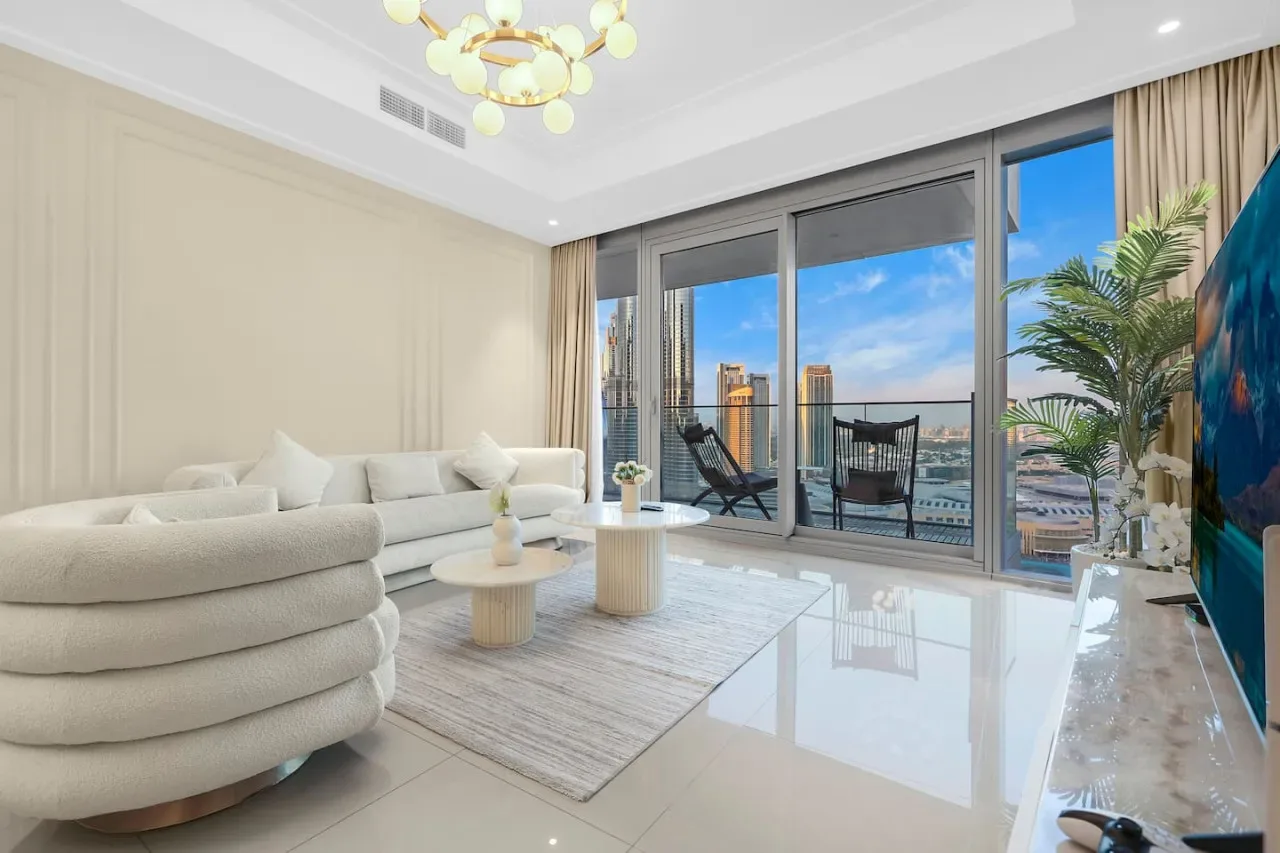 A bright living room with pale seating and large windows overlooking the city.