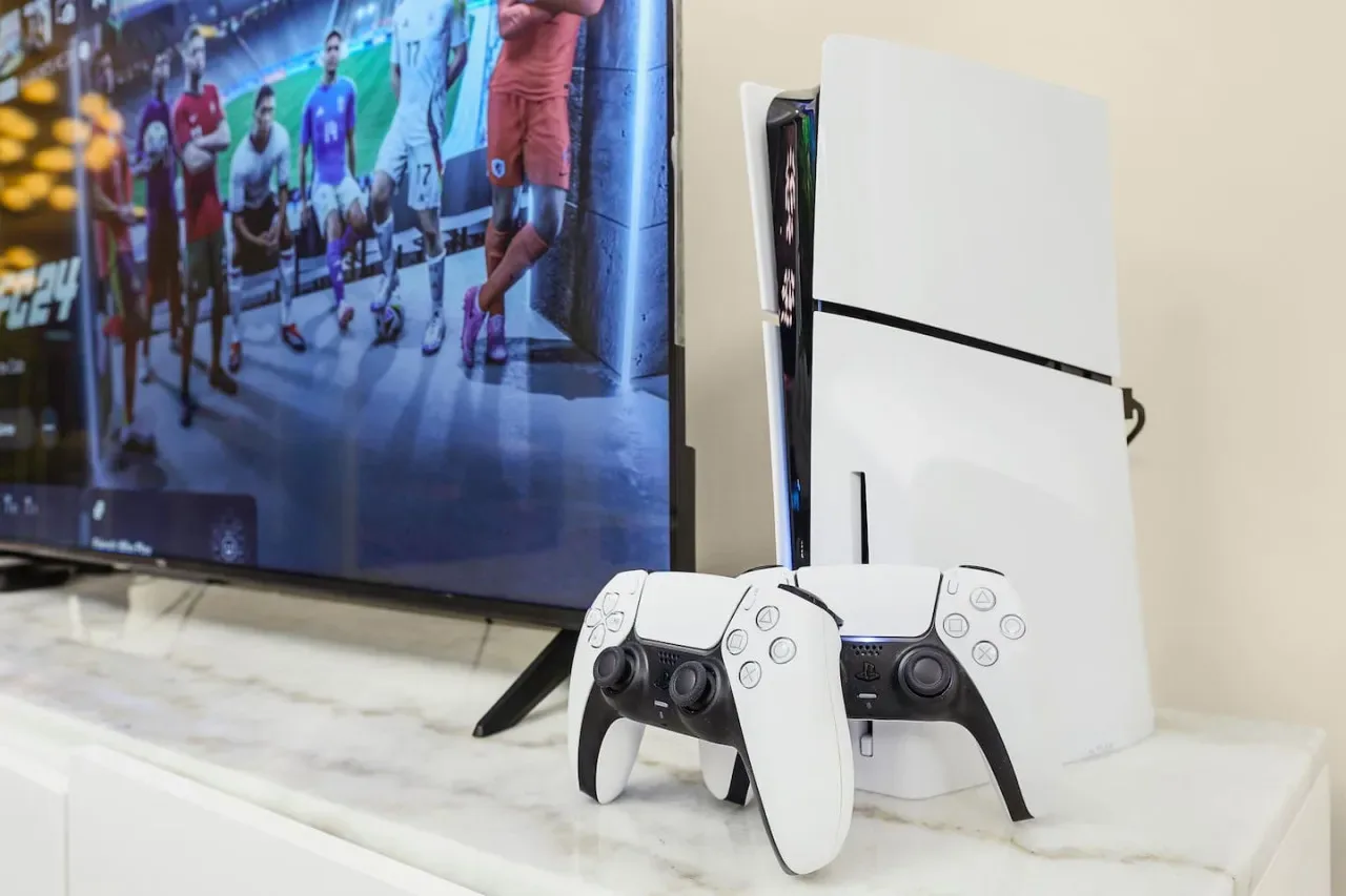 A game console and controller sit beside a television displaying a soccer game.