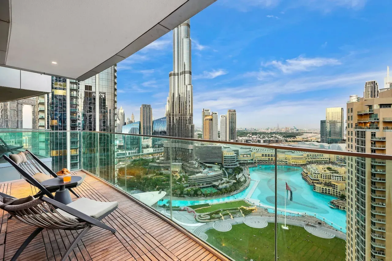 A balcony with seating overlooks a turquoise pool and surrounding city buildings.