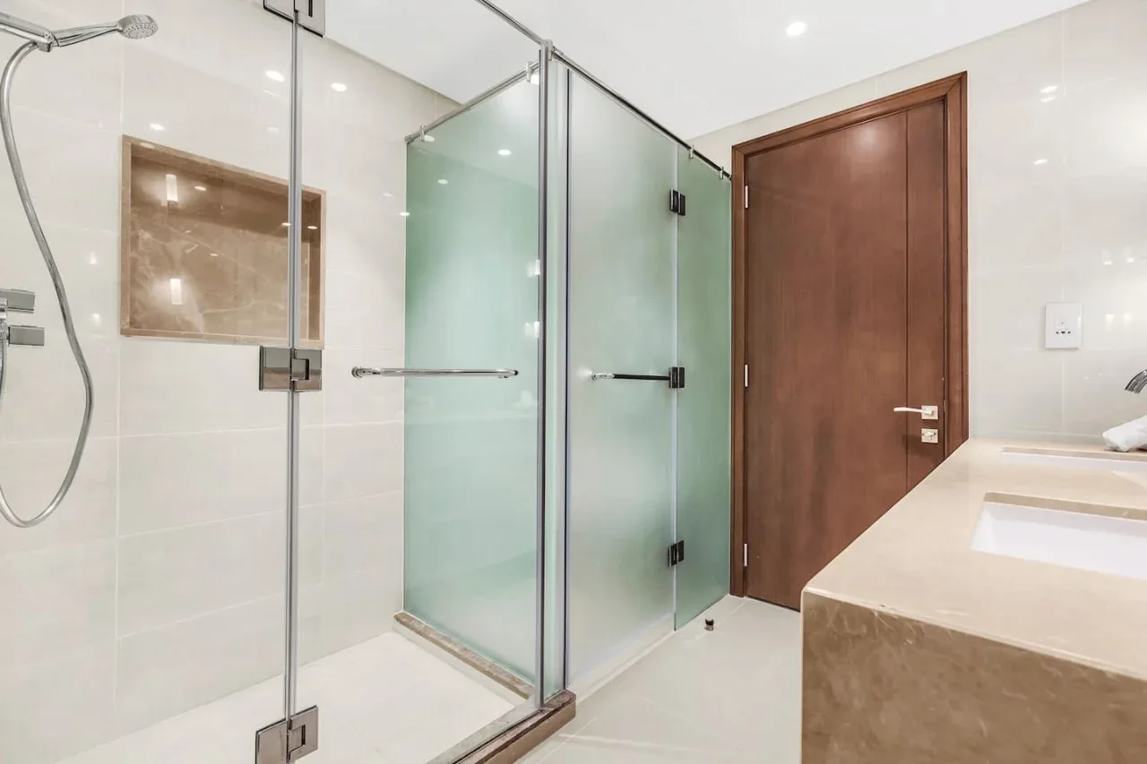 A tiled bathroom with a glass shower and a wooden door.