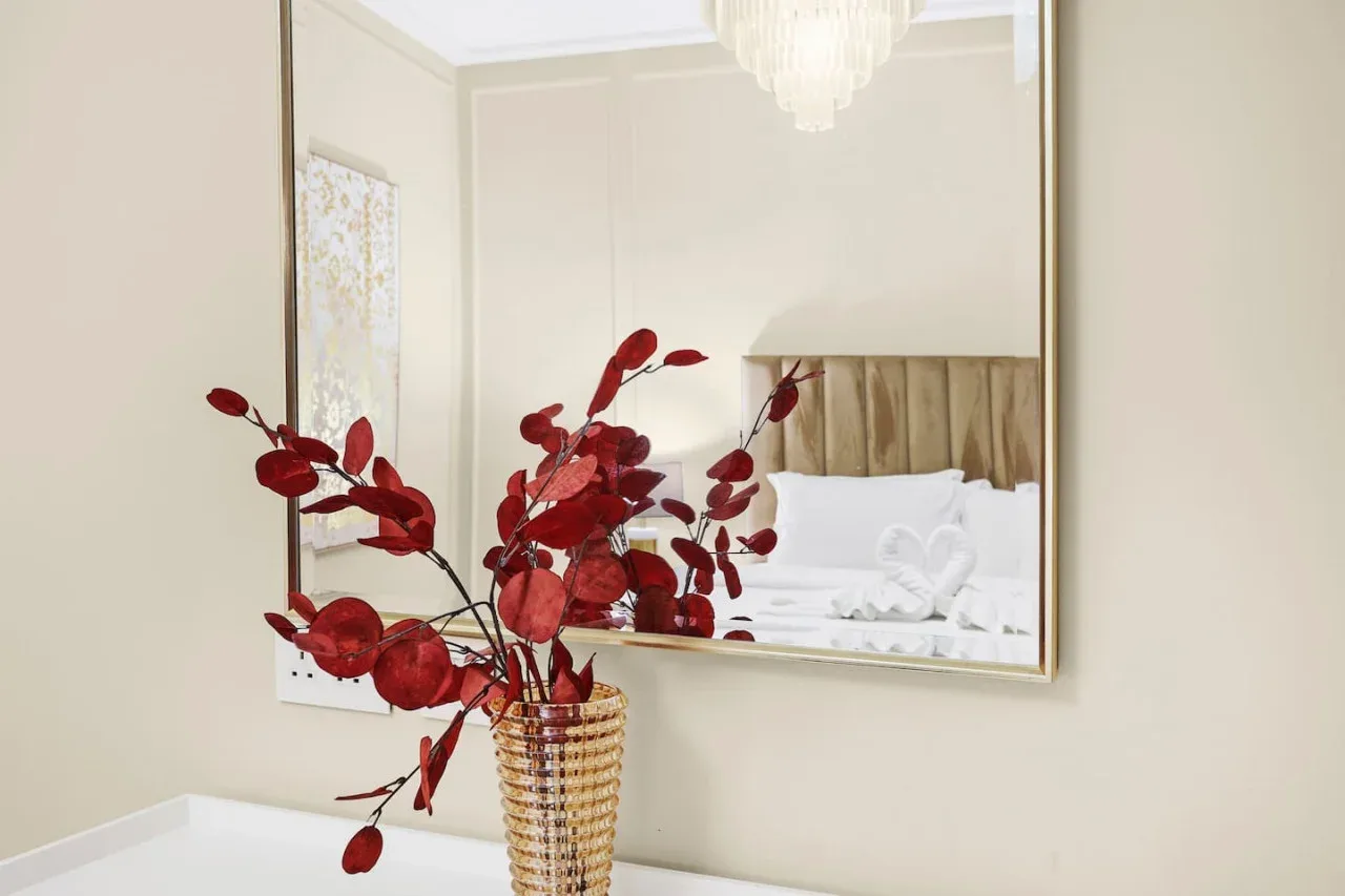 A bedroom with a bed reflected in a large wall mirror and red foliage in the foreground.