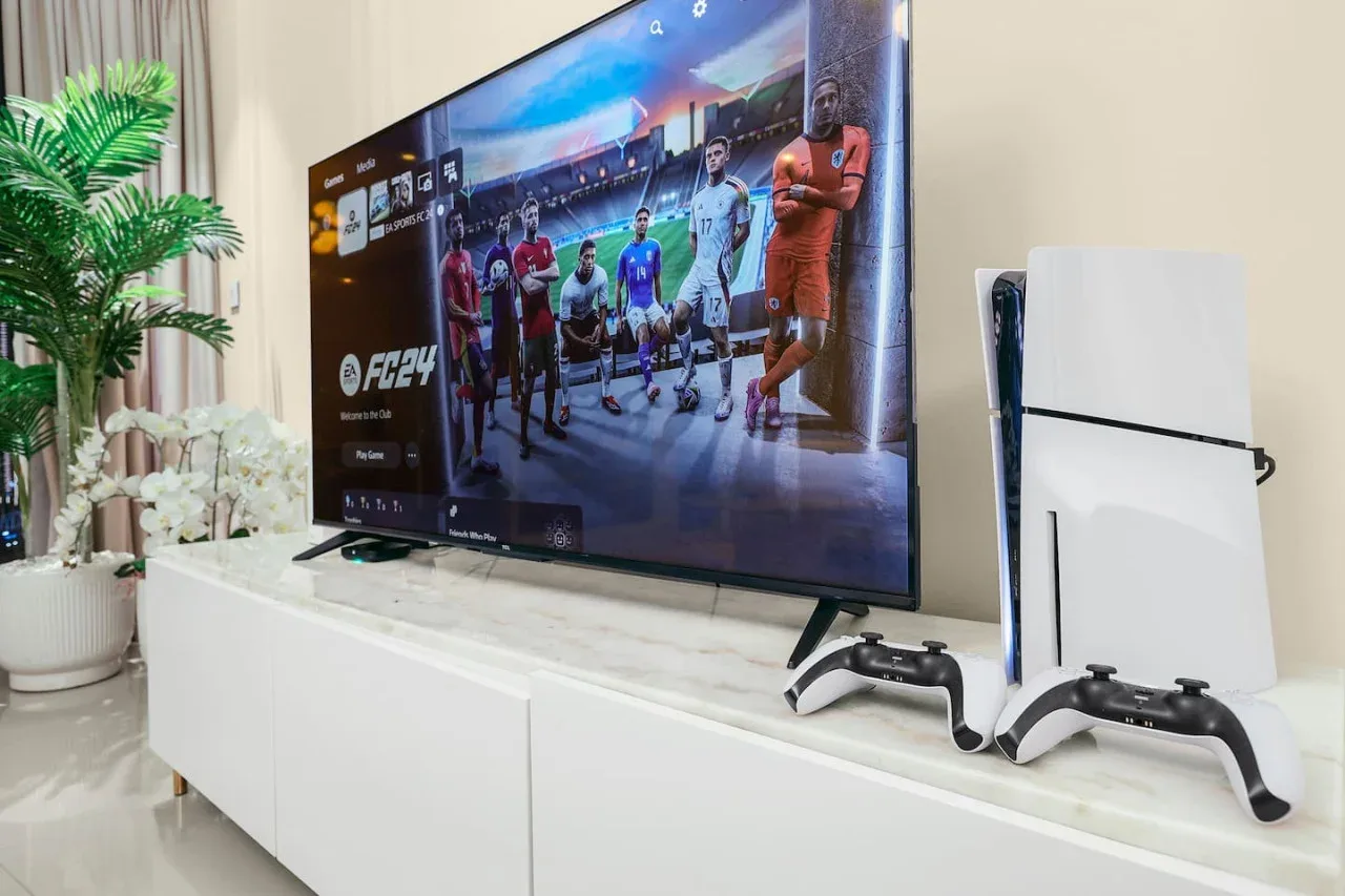A television displaying a soccer video game sits beside a game console on a white cabinet.