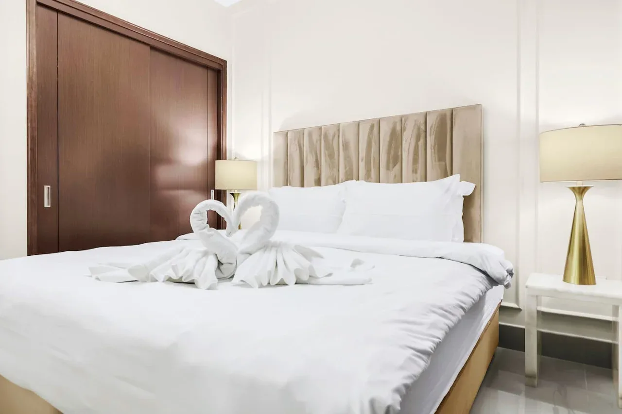 A bright bedroom with white bedding and folded towels arranged on the bed.