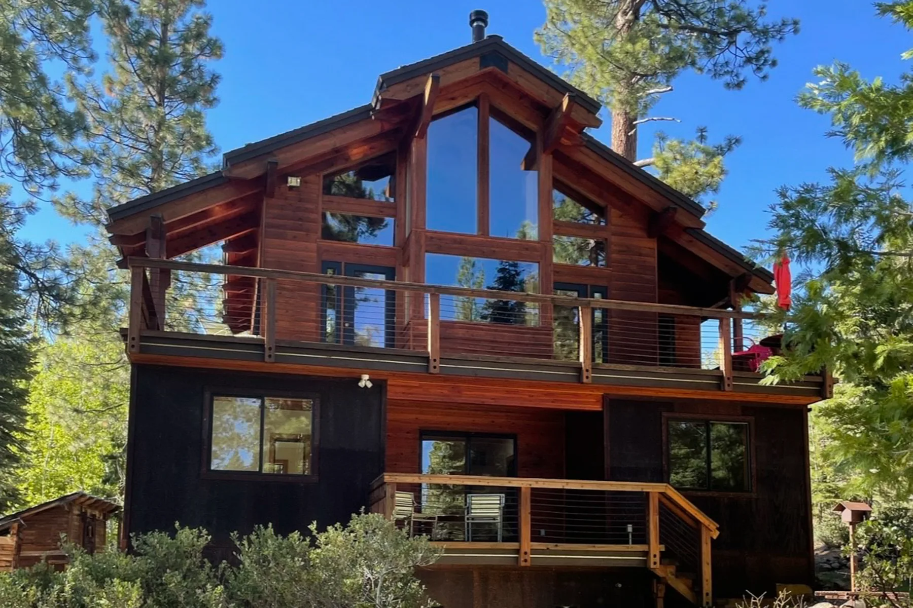 Una casa revestida de madera con grandes ventanas y un balcón entre árboles.