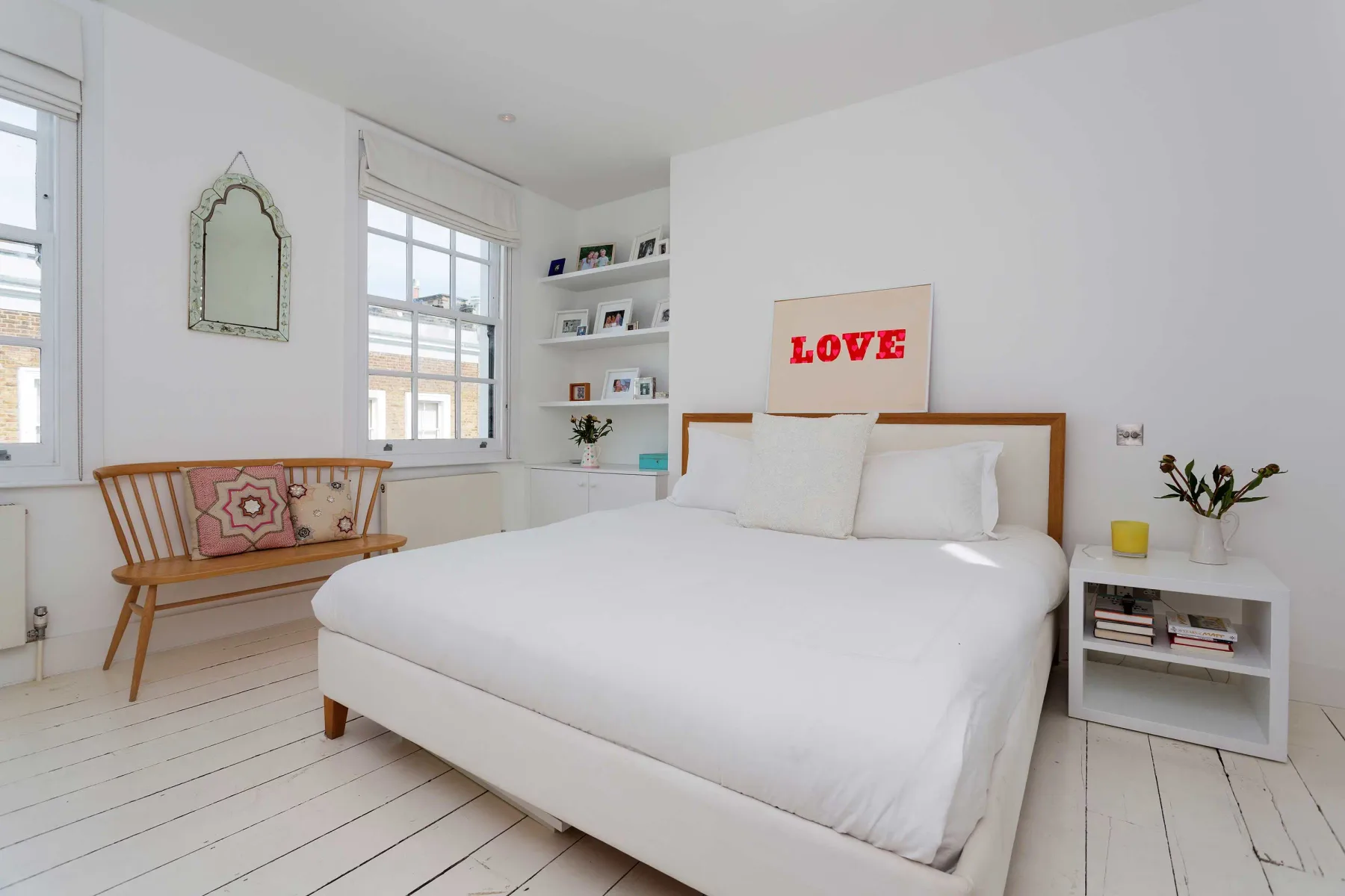 A bright bedroom with a white bed, windows, and built-in shelving.