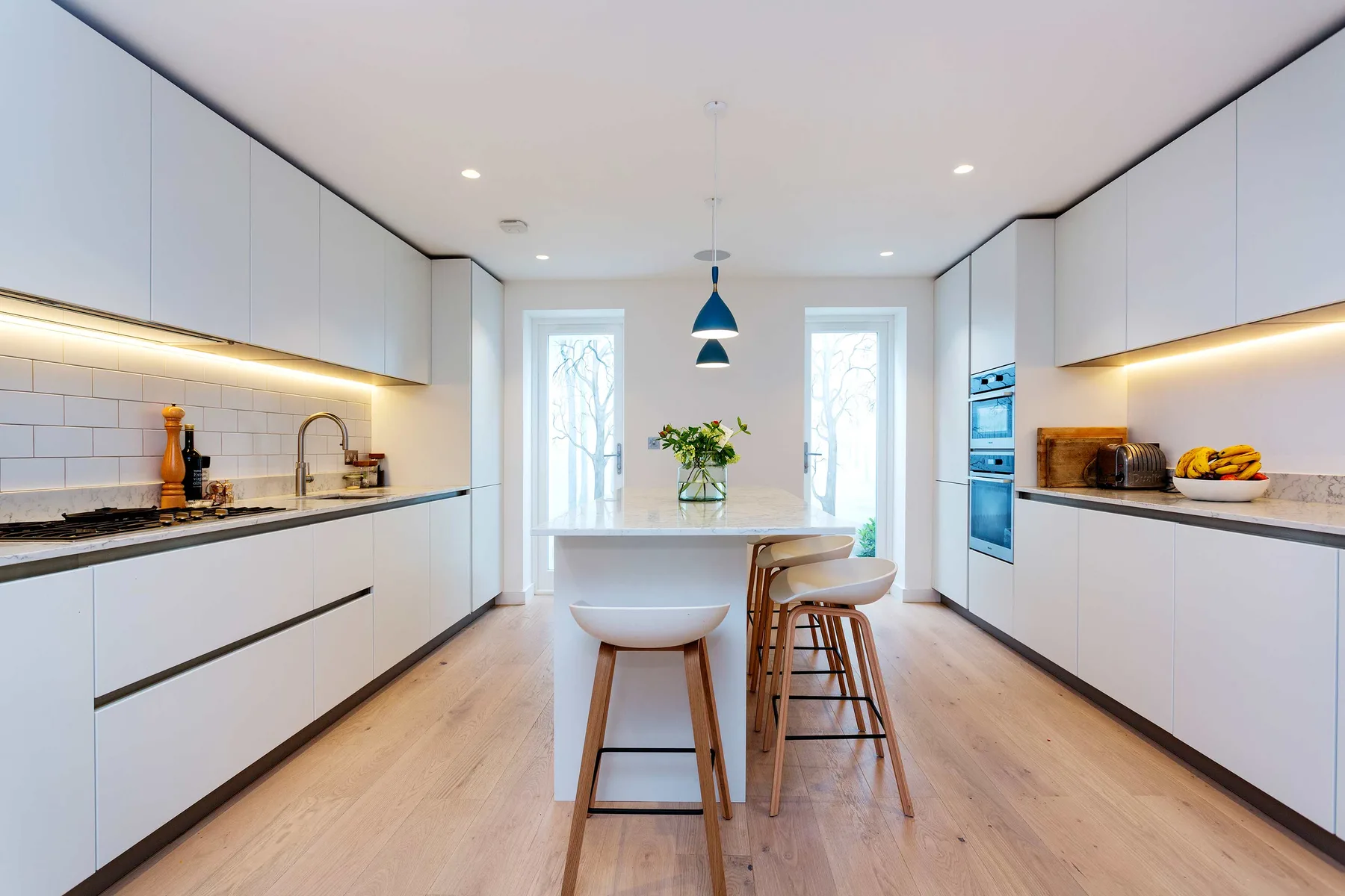 A bright modern kitchen with white cabinetry, a central island, and bar seating.