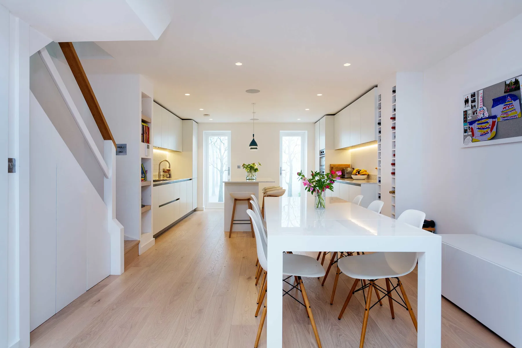 A bright open-plan kitchen and dining area with white cabinetry and a long dining table.