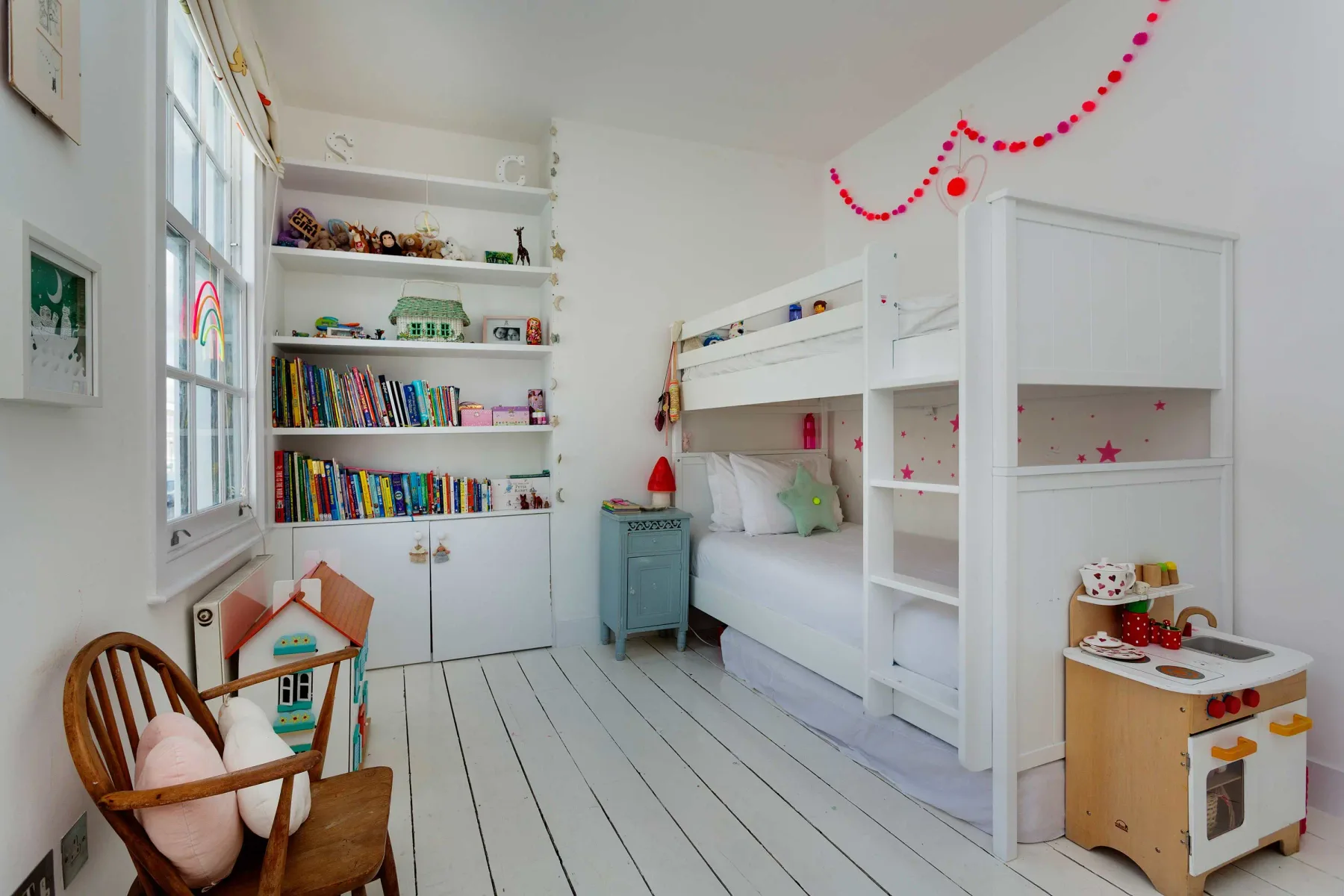A bright children’s bedroom with a bunk bed, bookshelves, and toys.