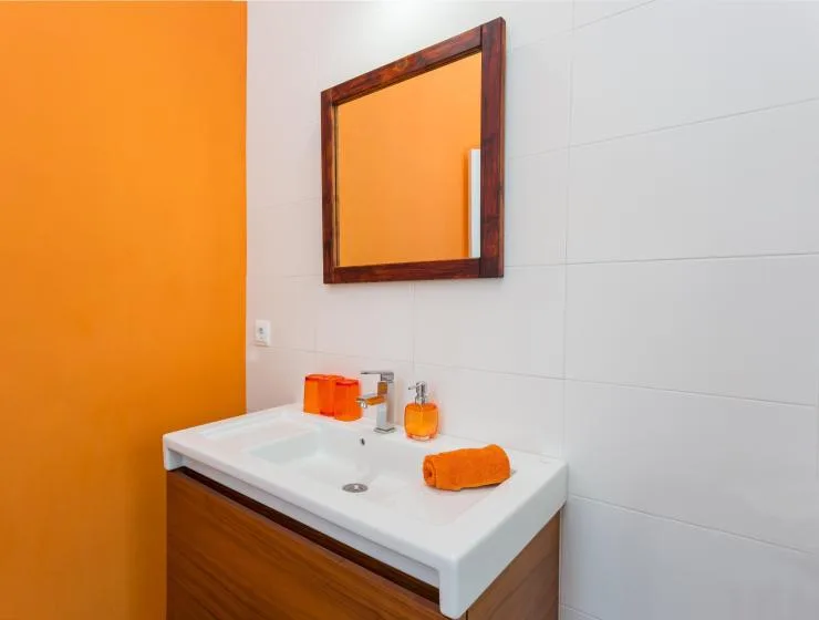 A bathroom vanity with a white sink, mirror, and orange accents.