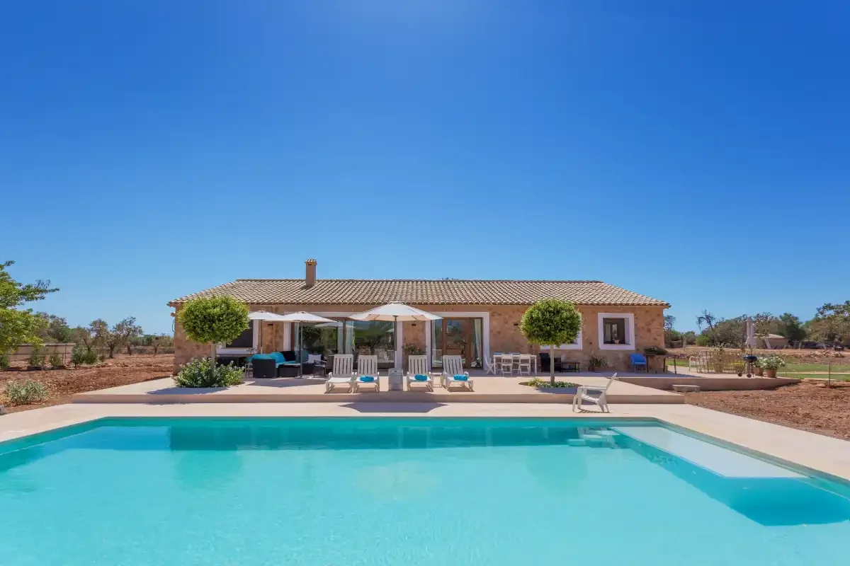 A single-story house faces a swimming pool and furnished patio.