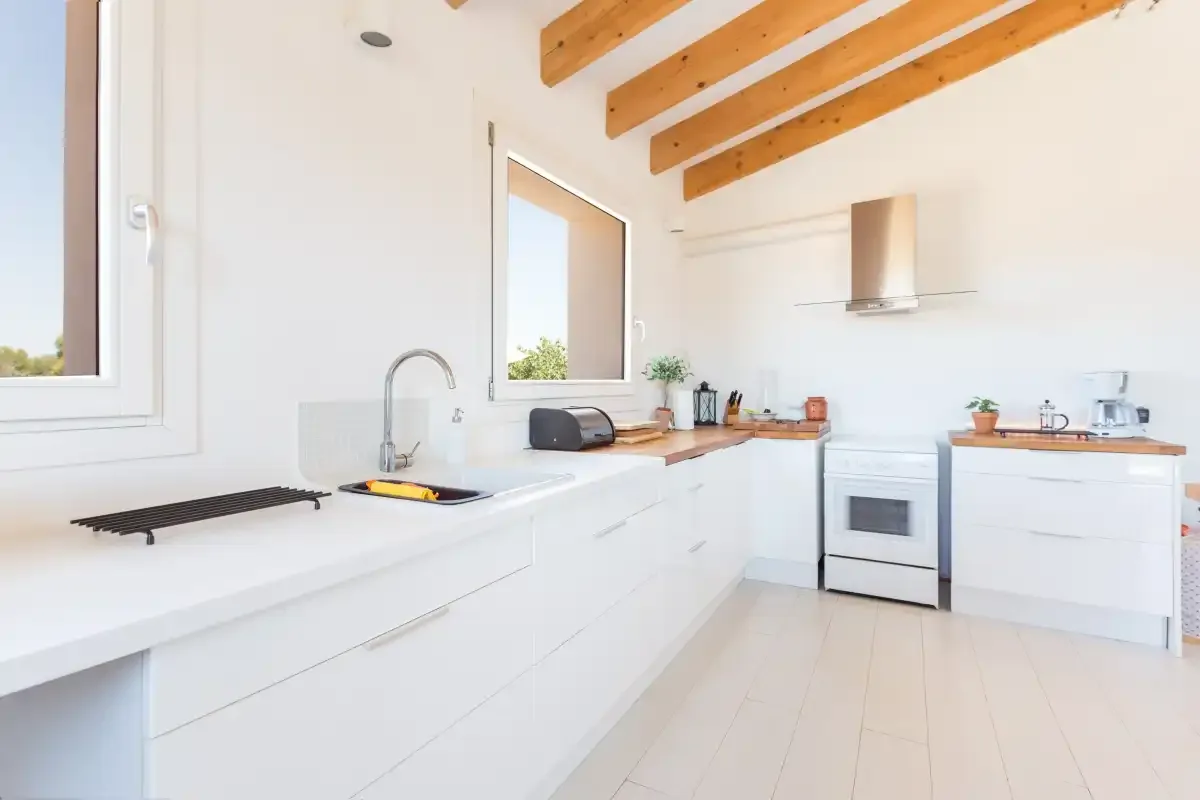 A bright kitchen with white cabinets, wooden ceiling beams, and a stove.