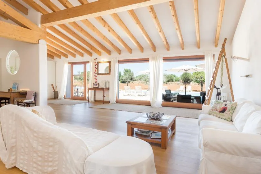 A bright living room with white seating and large windows opening onto a patio.