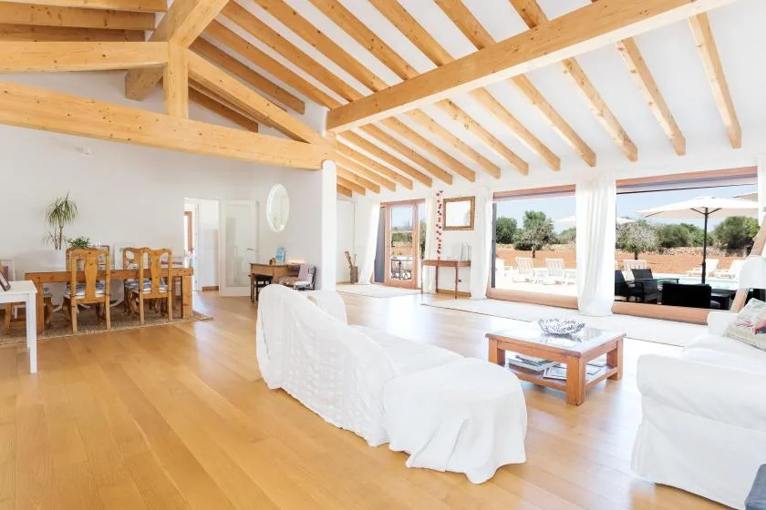A bright open-plan living and dining area with exposed wooden ceiling beams.