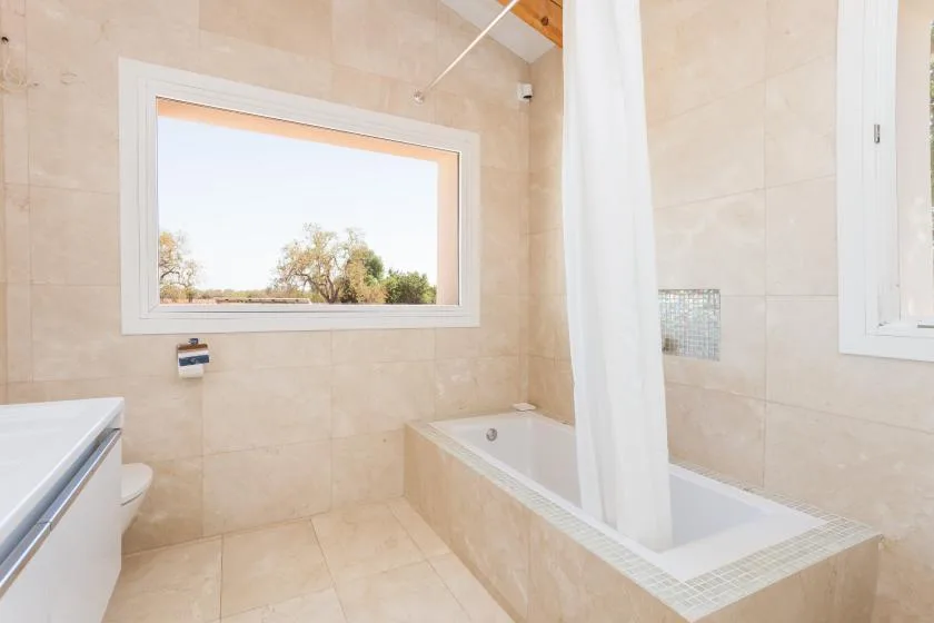 A tiled bathroom with a bathtub, shower curtain, and wide window.