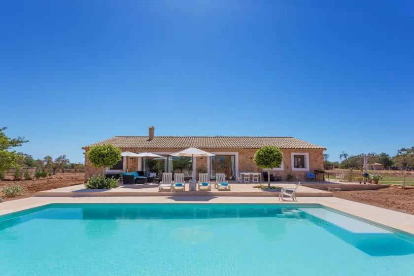 Una piscina frente a una casa de una planta bajo un cielo azul despejado.