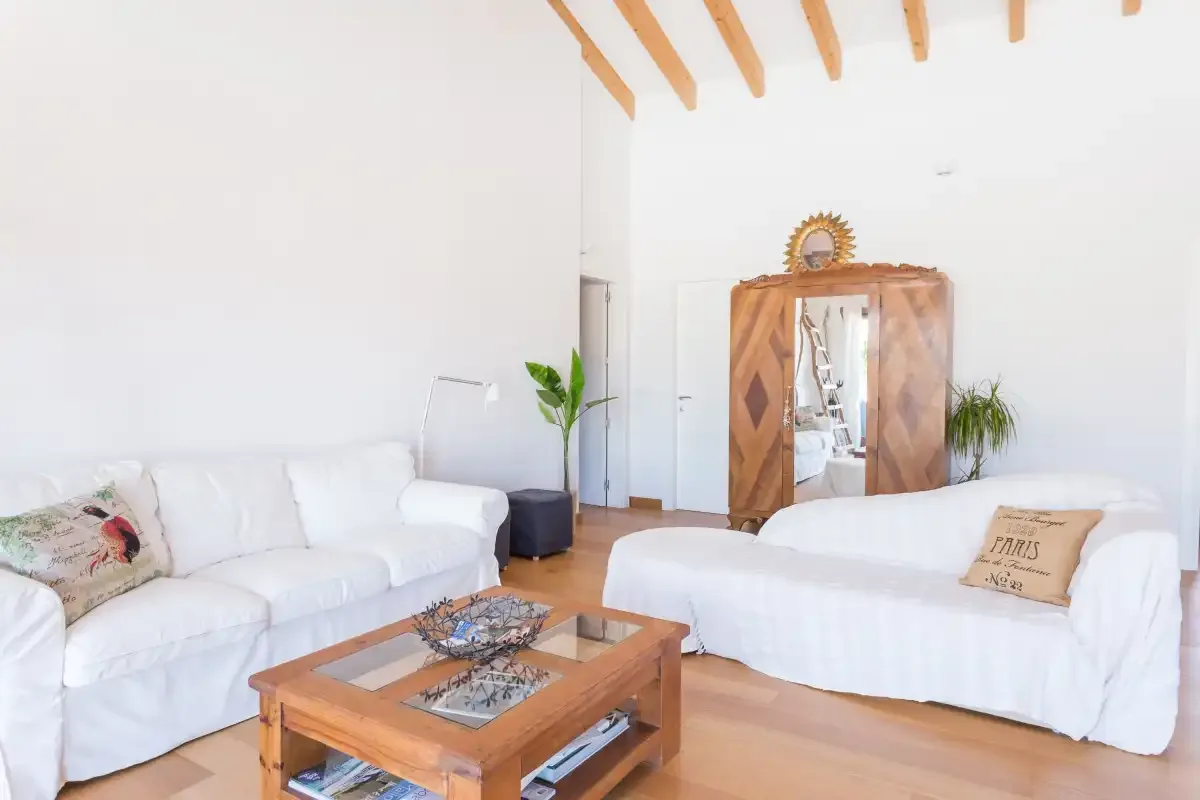 A bright living room with white seating, a wooden coffee table, and exposed ceiling beams.