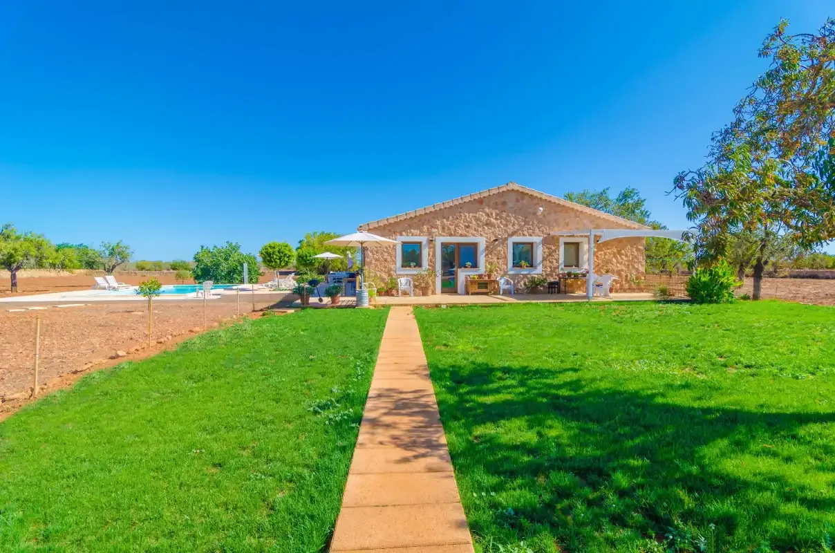 A stone house stands beyond a path crossing a green lawn.