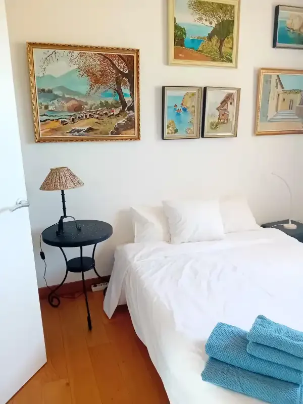 A bedroom with a white bed, framed artwork, and a bedside table.