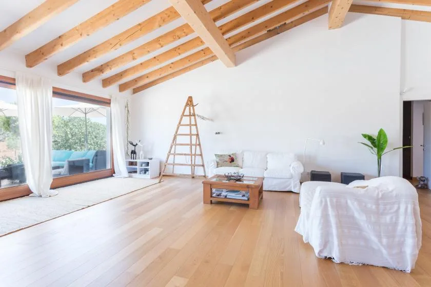 A bright living room with white seating and exposed wooden ceiling beams.