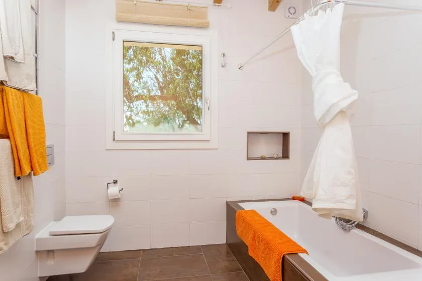 A bathroom with a bathtub, orange towels, and a window.