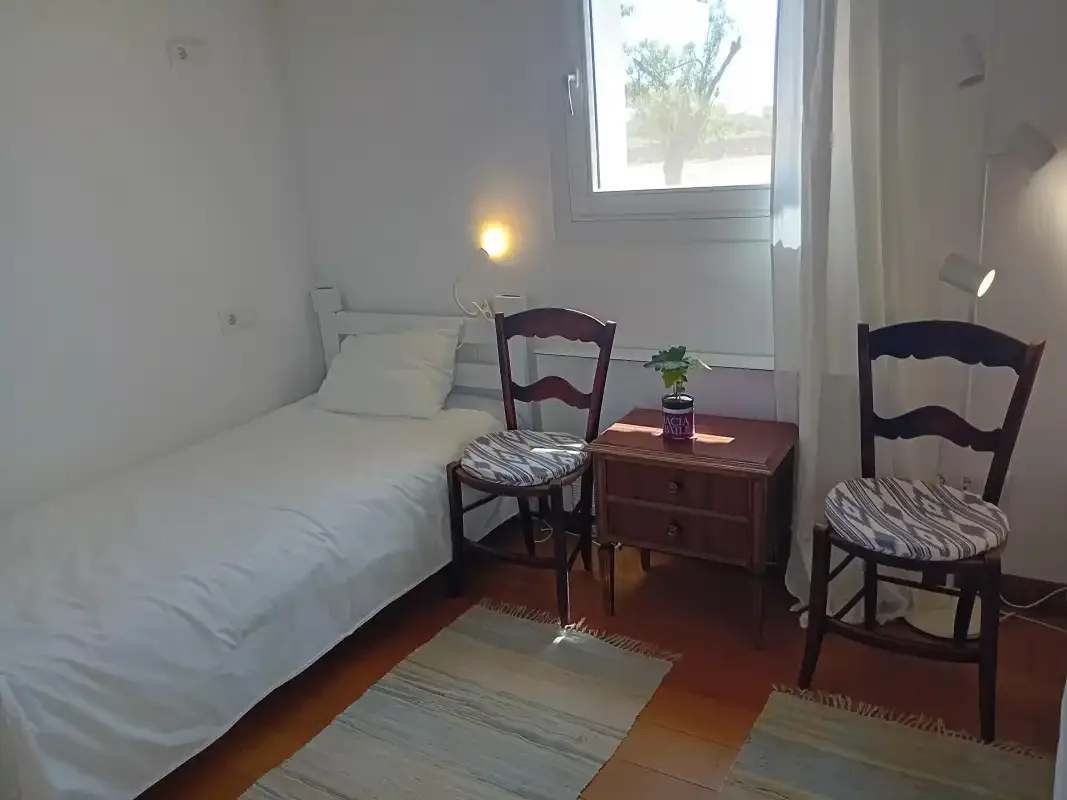 A bedroom with a single bed, two chairs, and a small bedside table.