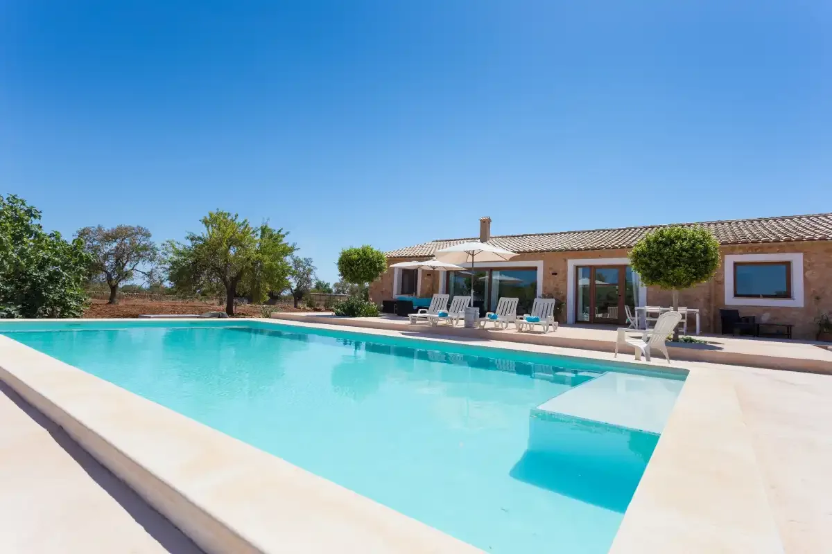 A swimming pool beside a single-story house under a clear blue sky.