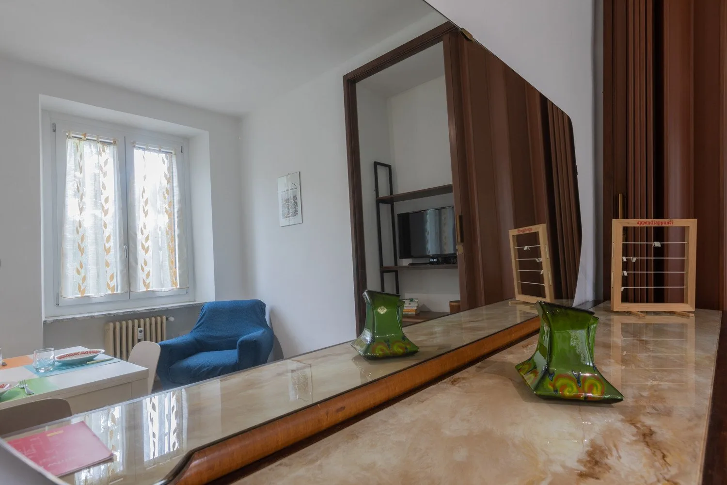 Una sala de estar con un sillón azul junto a una ventana y una mesa larga con espejo.