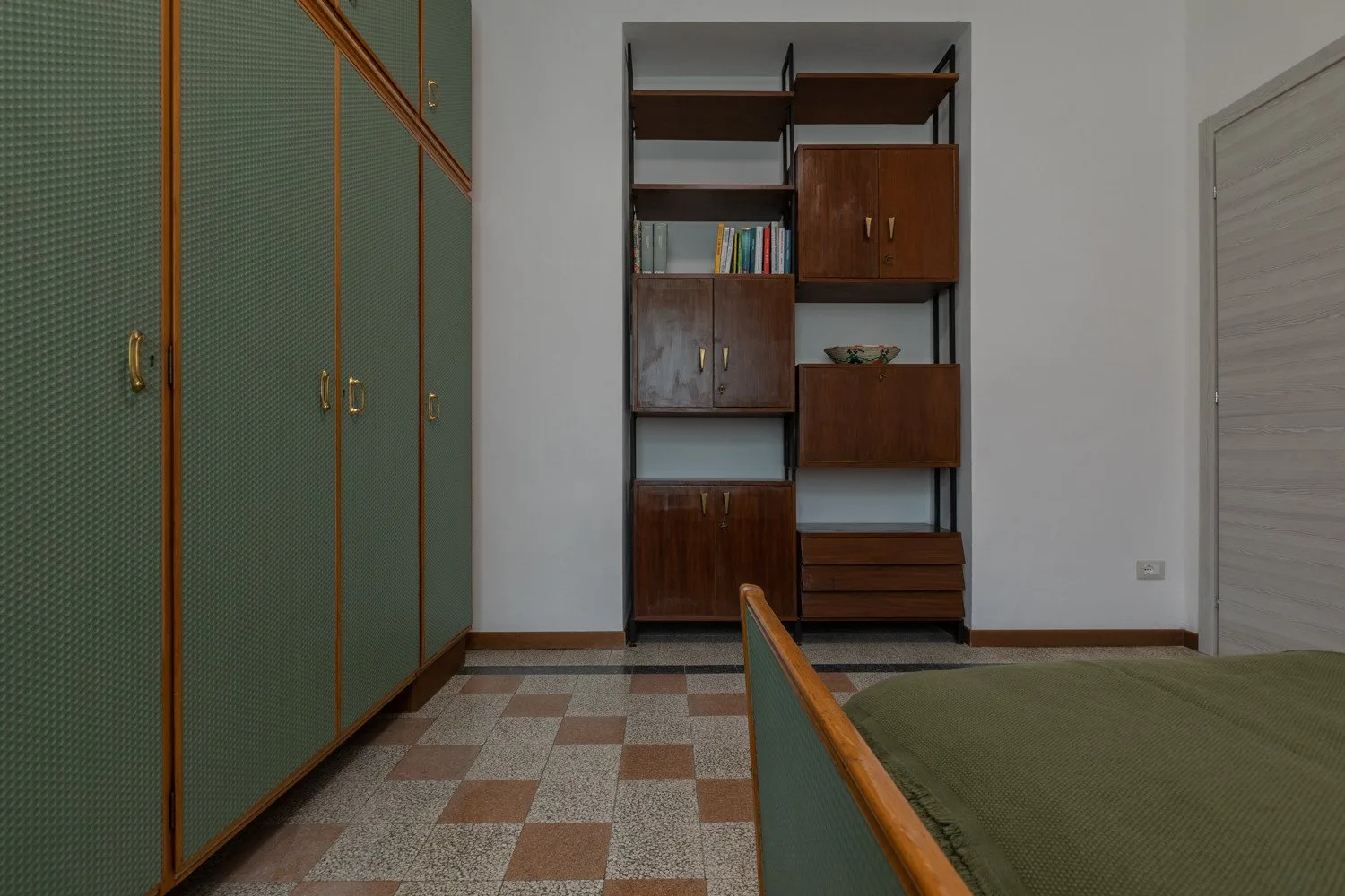 Dormitorio con armarios verdes y una cama junto a estanterías de madera empotradas.